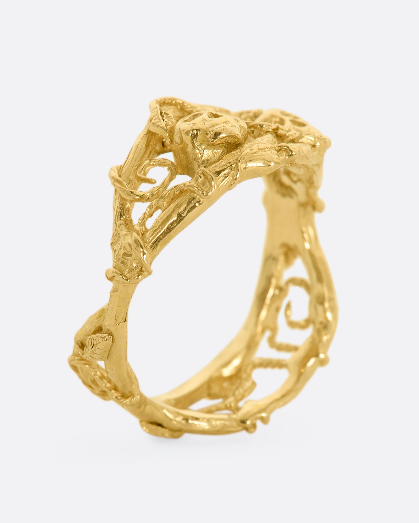 A yellow gold momento mori ring with organic branch and vine motif, featuring two skulls. View standing, from the side.