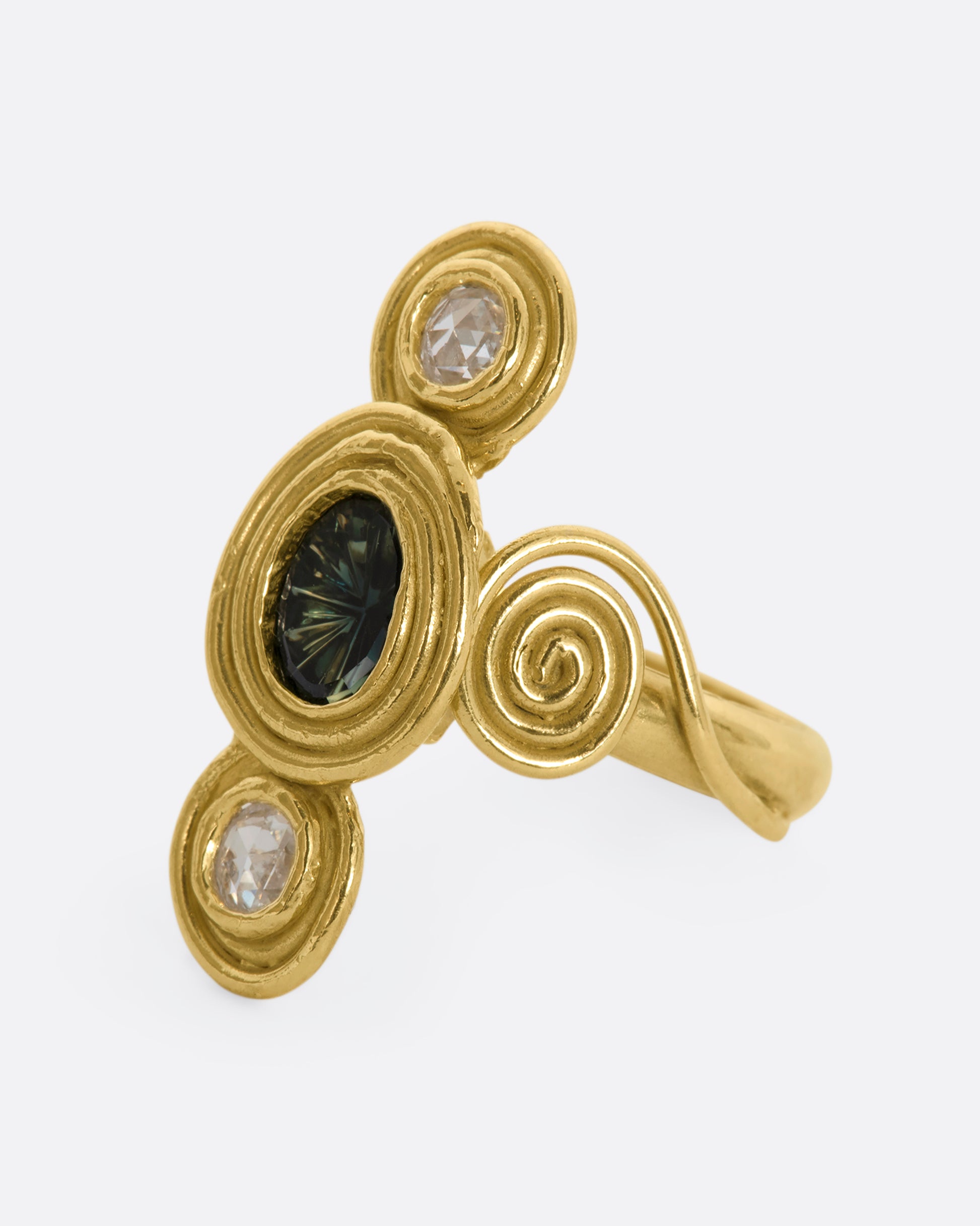 A yellow gold ring with circle and spiral motifs. At the center is a parti-color Australian sapphire with a rose cut diamond above and below. View from the side.