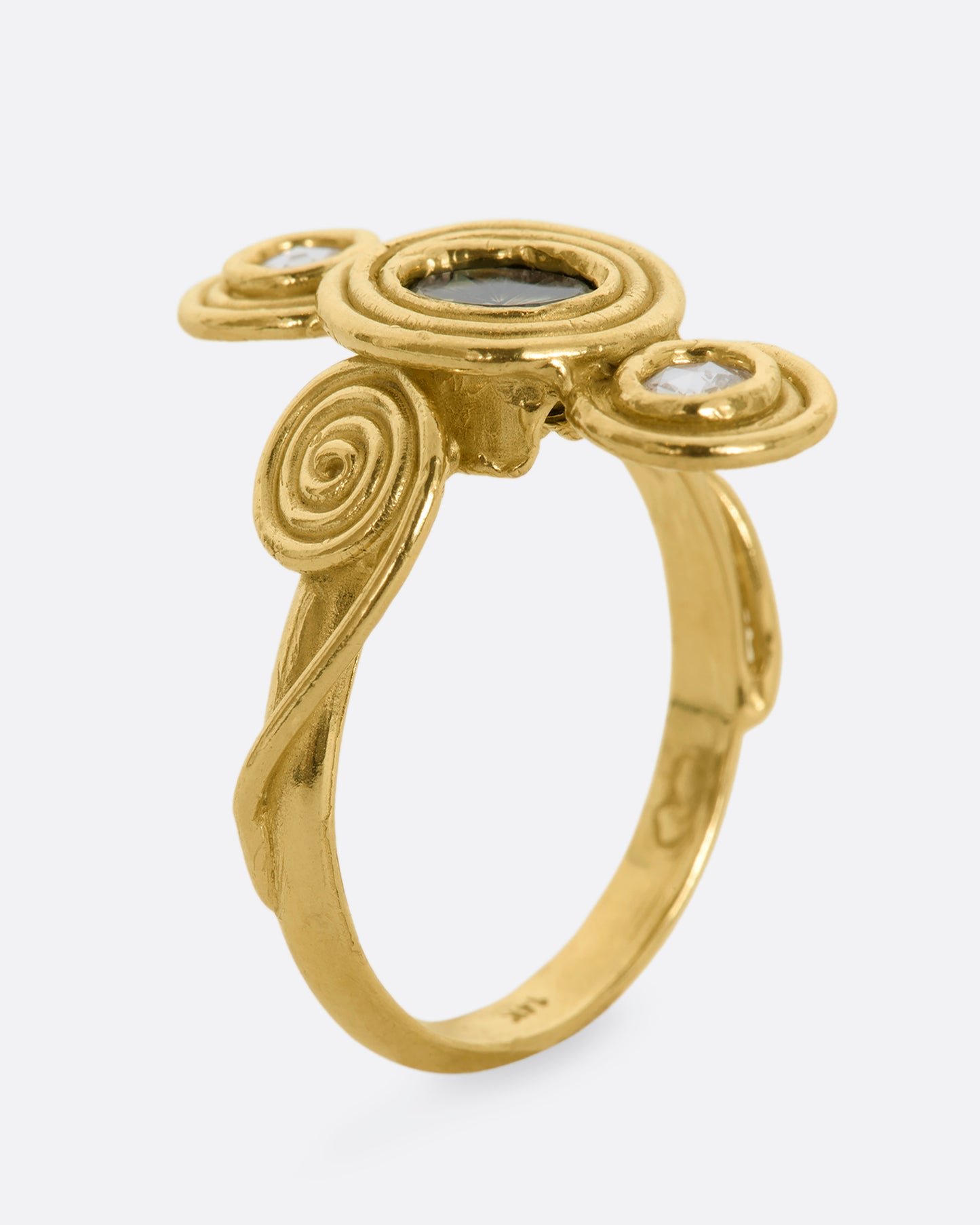 A yellow gold ring with circle and spiral motifs. At the center is a parti-color Australian sapphire with a rose cut diamond above and below. View from the side, standing up.