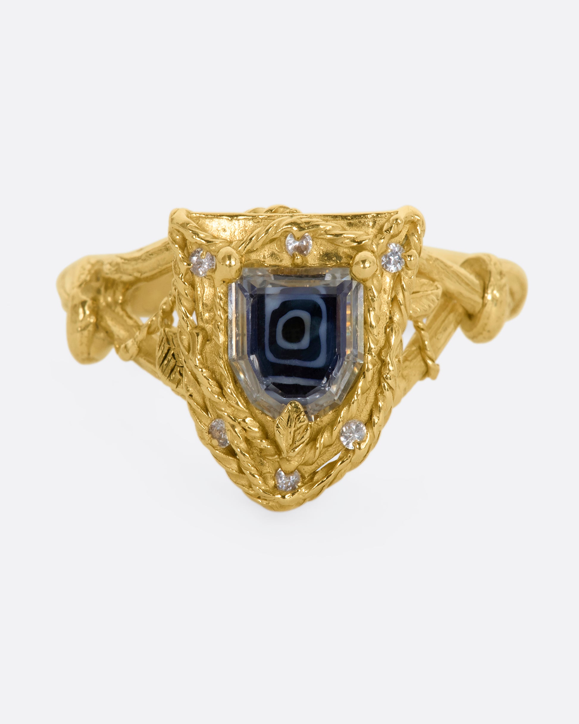 A yellow gold shield shaped ring with vine motif and a geometric portrait cut sapphire over Italian micromosaic glass with brilliant cut white sapphires in a halo around. View from the front.