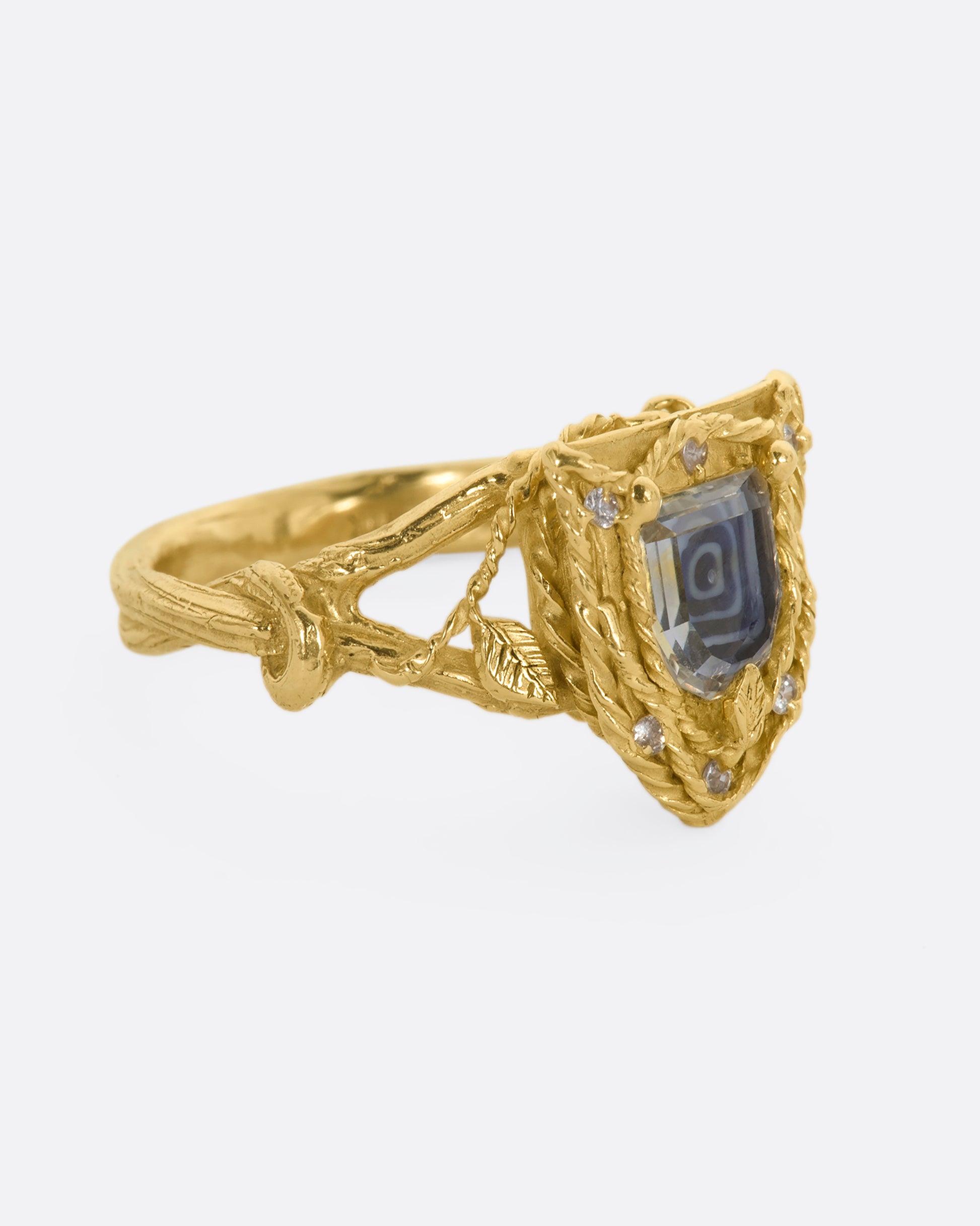 A yellow gold shield shaped ring with vine motif and a geometric portrait cut sapphire over Italian micromosaic glass with brilliant cut white sapphires in a halo around. View from the alternate side.