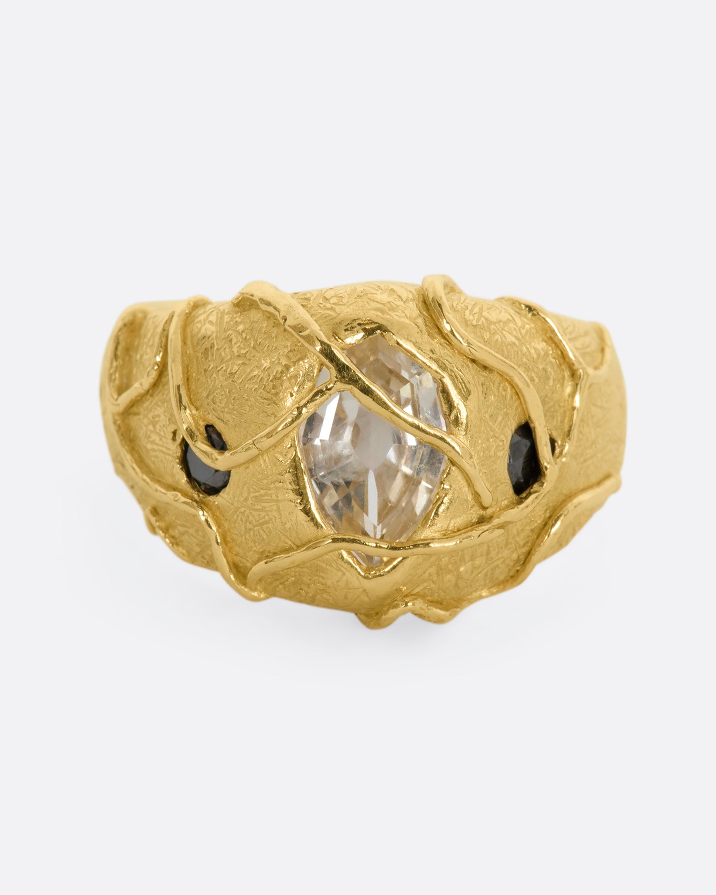 A chunky yellow gold ring with a vine motif that looks like it's grown over the fancy step cut sapphire at the center and the brilliant black diamonds. View from the front.