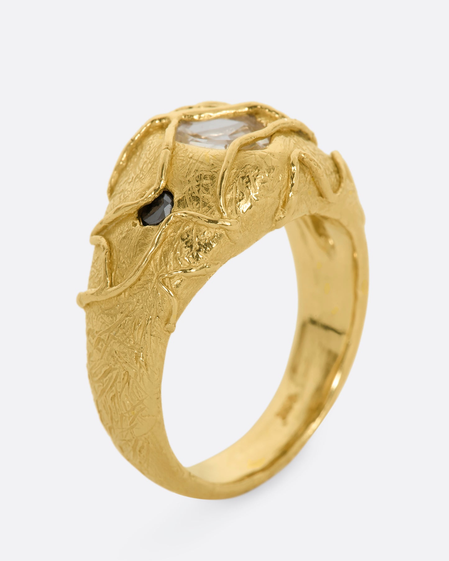 A chunky yellow gold ring with a vine motif that looks like it's grown over the fancy step cut sapphire at the center and the brilliant black diamonds. View from the side, standing up.