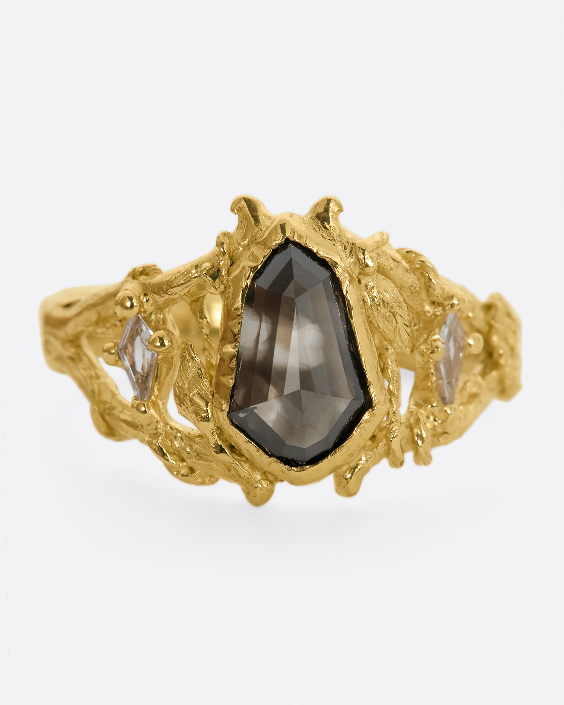 A yellow gold ring with an organic vine motif and a shield double cut black diamond at the center with white kite sapphires on either side. View close up of the diamond.