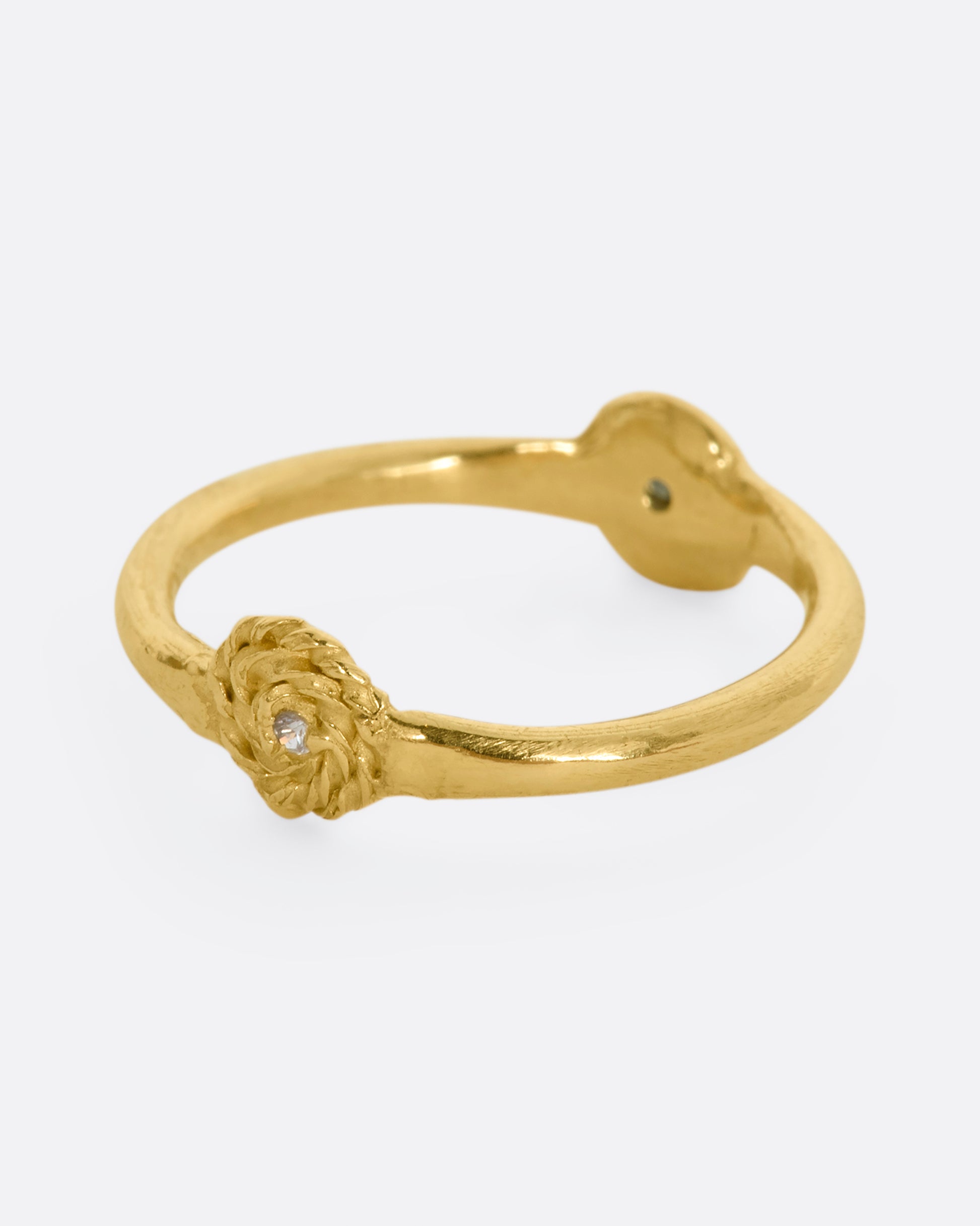 A yellow gold ring with a rosebud motif on either side, one with a white sapphire, the other with a blue sapphire for wear two ways. Side view.