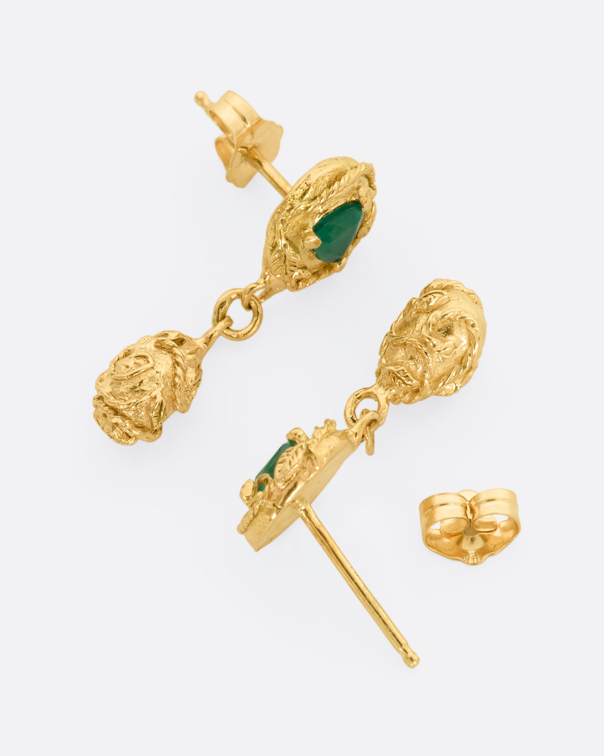 A pair of yellow gold drop earrings with vine motif and a trillion cut emerald on each. View from above, laying flat.