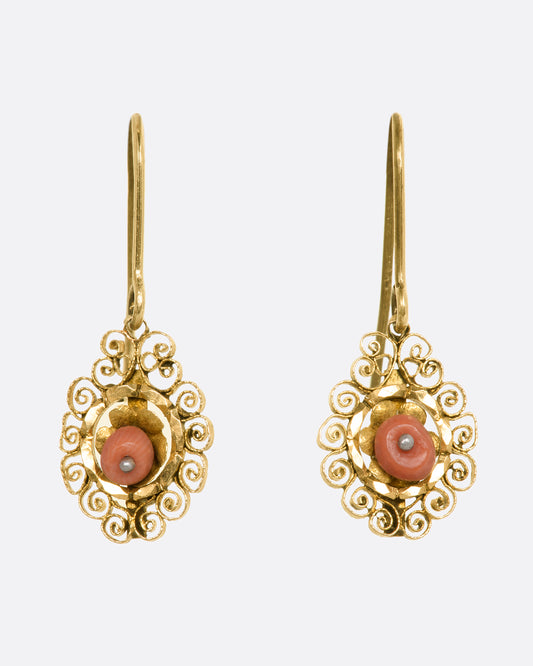 Yellow gold drop earrings with a coral beads surrounded by a filigree halo. View from the front.