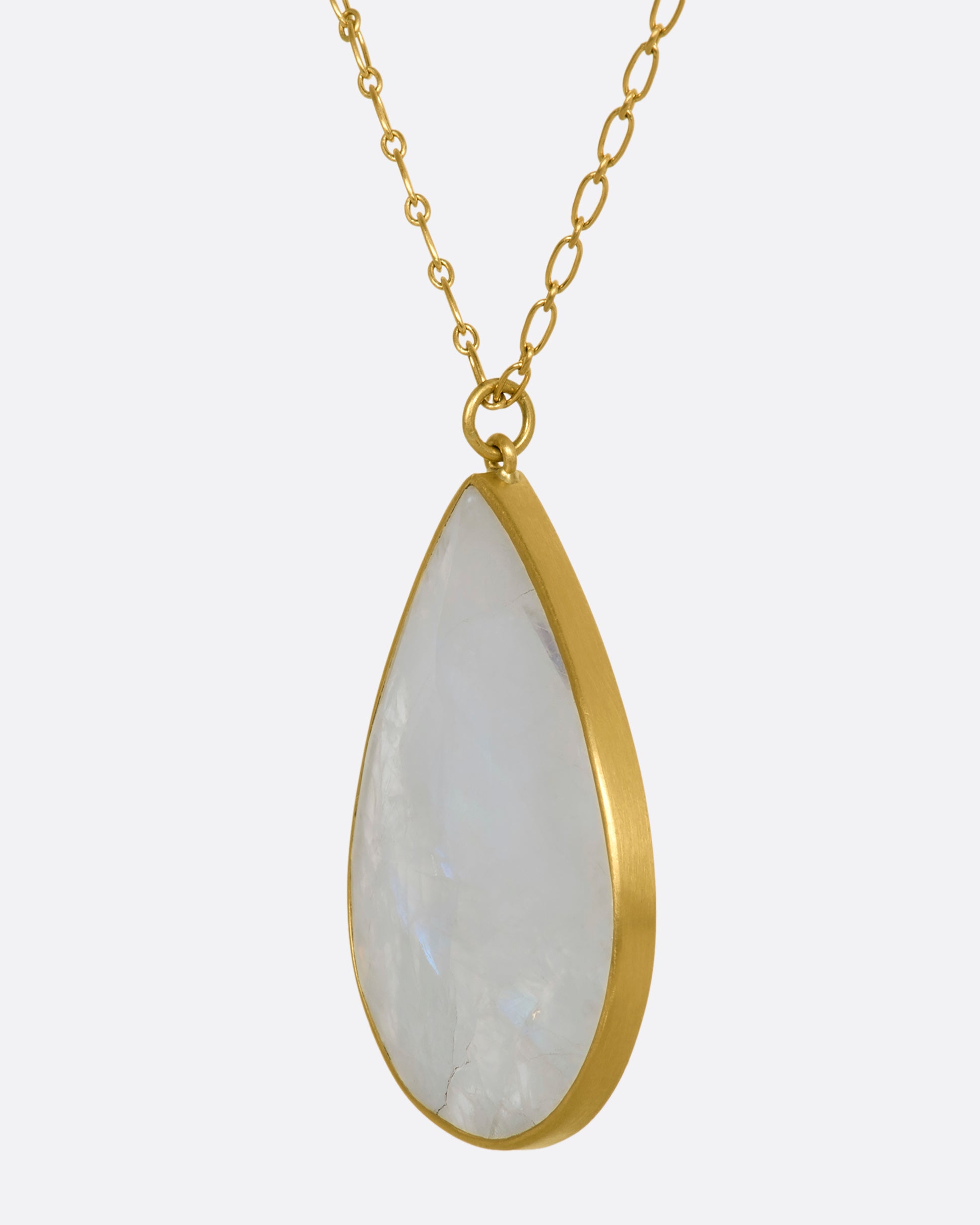 A tear drop shaped moonstone in a yellow gold bezel setting hanging from a yellow gold chain. View up close from the side.