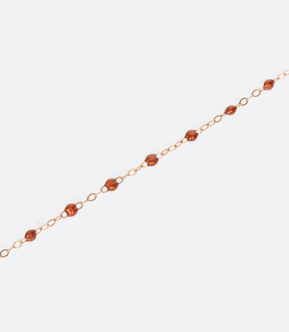A close up view of a yellow gold cable chain necklace with rusty red resin droplets. Shown from the side.