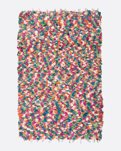 A bird's eye view of a green, red, orange, and white rectangular rag rug.