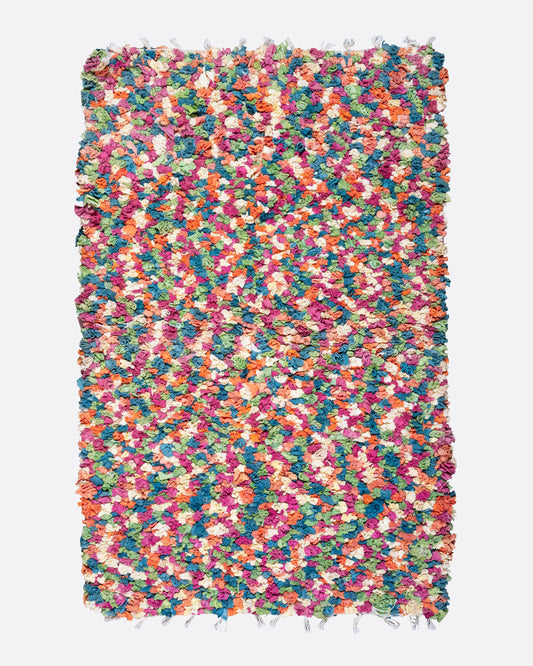 A bird's eye view of a green, red, orange, and white rectangular rag rug.