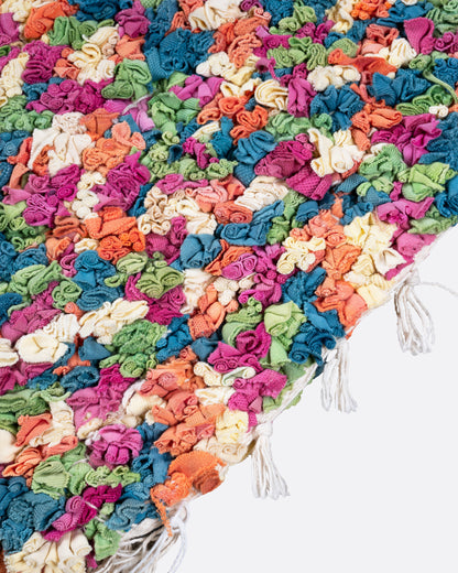 A close up of  green, red, orange, and white rectangular rag rug.