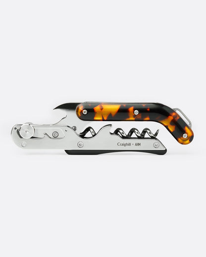 A wine key and bottle opener combo with a tortoiseshell handle and silver metal components, shown horizontally.