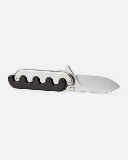 A stainless steel pocket knife with an interlocking mechanical hilt that moves with the blade and black handle, shown open from the side.