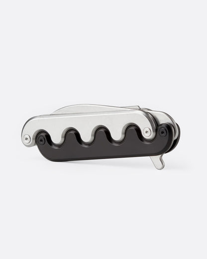 A stainless steel pocket knife with an interlocking mechanical hilt that moves with the blade and black handle, shown from the side.