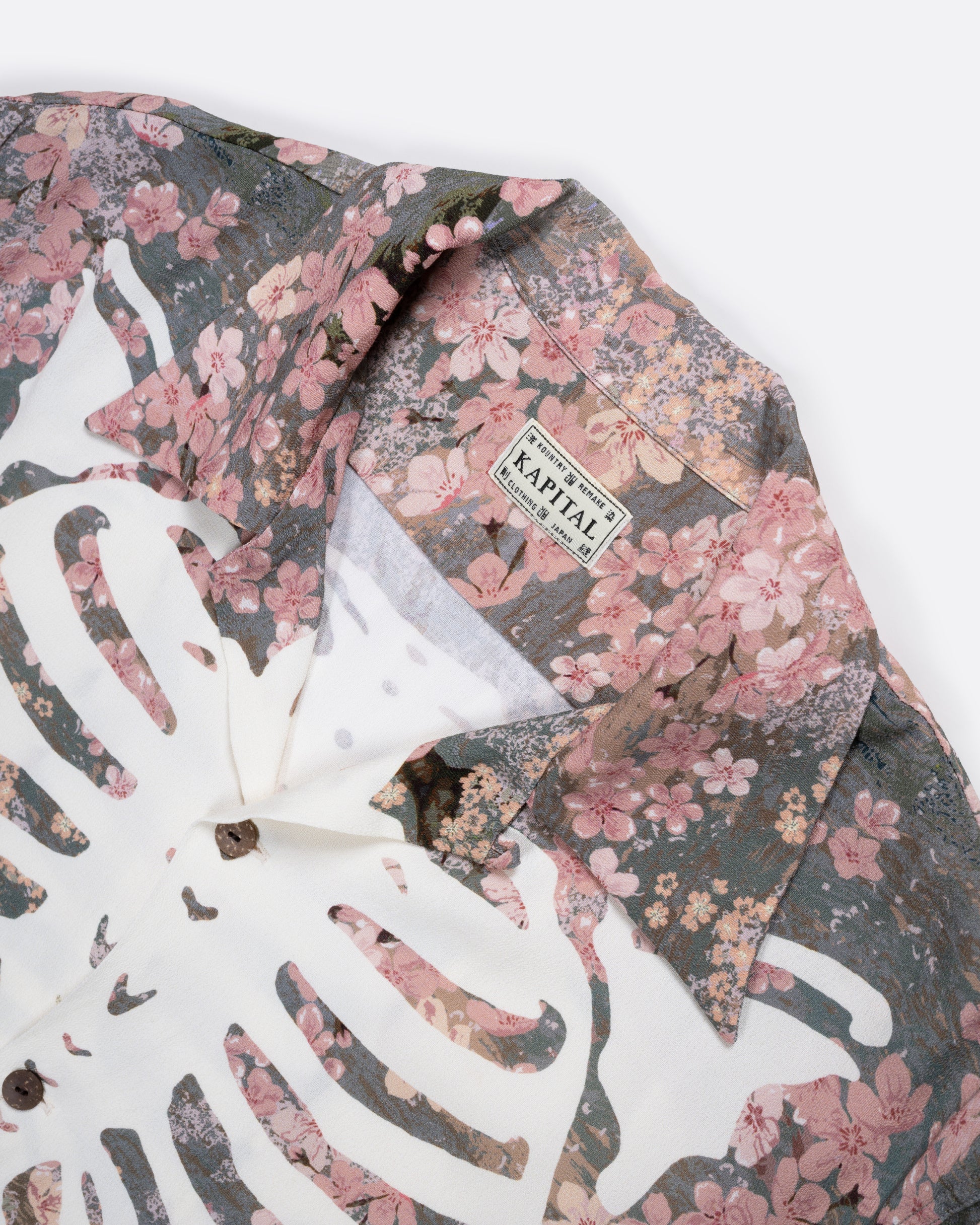 A close up of the collar of a button front short sleeve shirt with a cherry blossom print punctuated by Kapital’s skeleton motif.