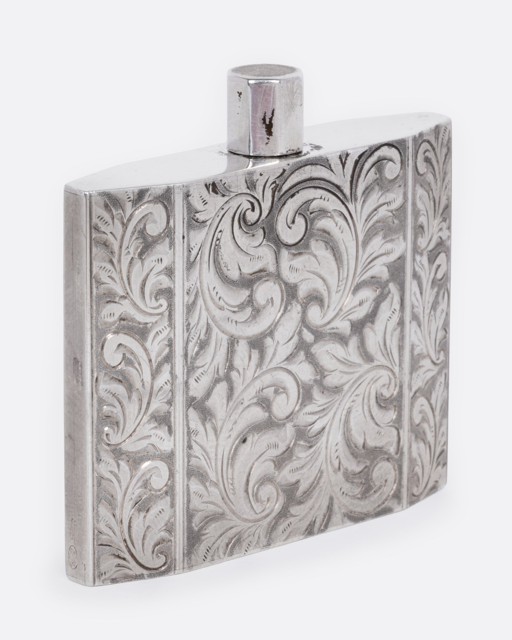 A silver perfume bottle with winding botanical etchings and a slim square silhouette, shown from the side.