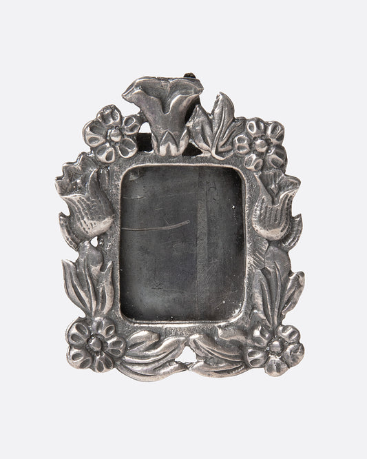 An ornate  silver picture frame brooch with a botanical motif around a rectangular opening, shown from the front.