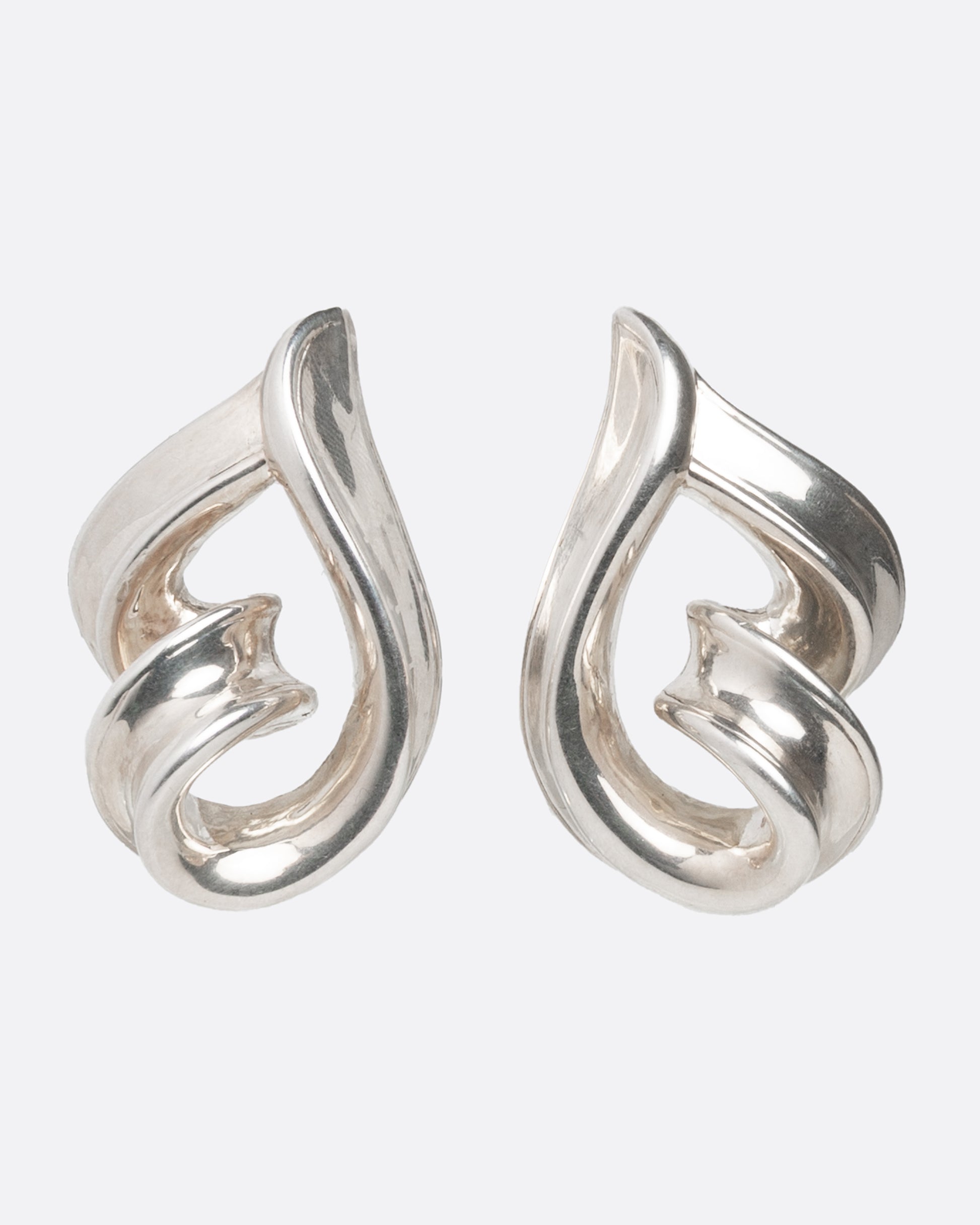 A pair of twisting silver loop earrings shown from the front.