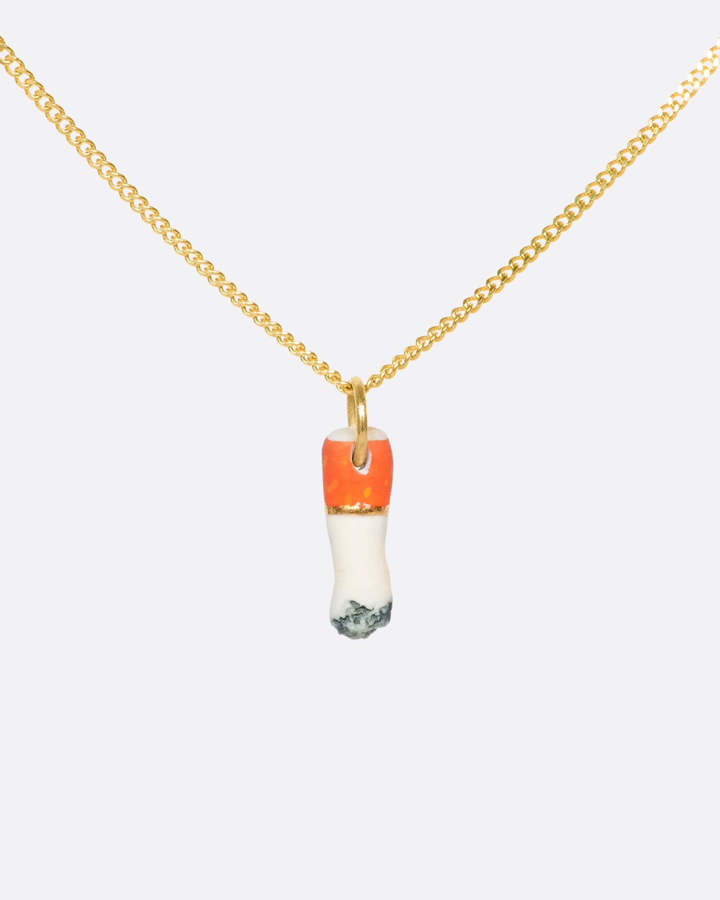 A view of a porcelain cigarette charm on a yellow gold bail hanging on a gold chain.