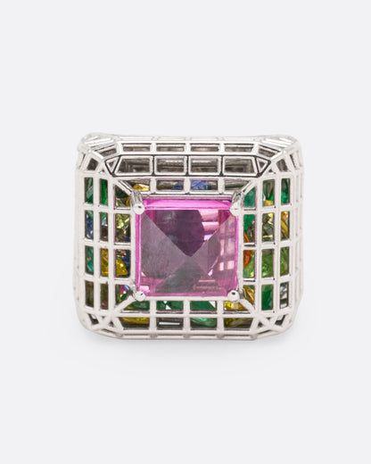 White gold and pink sapphire cage ring, top view of the pink sapphire framed by a grid of green, blue and yellow stones