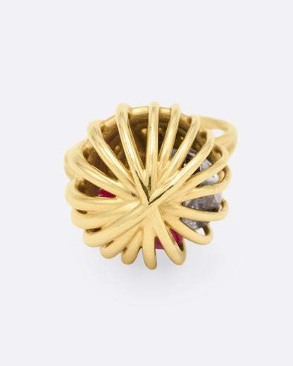 Yellow gold cage ring with loose ruby and sapphires, top view of the cage, gold wires meeting at the center over the loose stones