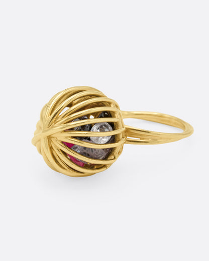 Yellow gold cage ring with loose ruby and sapphires, angled view of the cage with the ruby and white sapphire visible inside