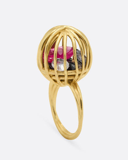 Yellow gold cage ring with loose ruby and sapphires, side view of the Rattled ring showing the round wire cage set on a slim double band