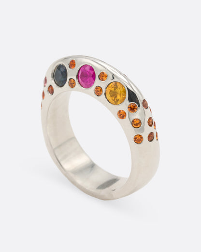 A dimensional sterling silver ring with orange, blue, and pink sapphires on either side, shown from the side standing up.
