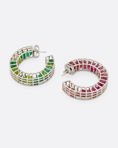A silver pair of caged hoop earrings filled with loose emeralds, peridots, rubies, and topaz, shown from the side.