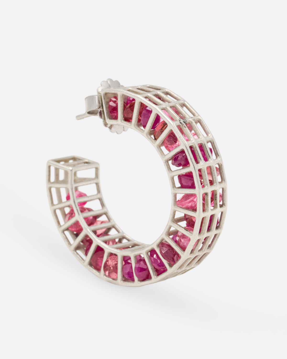 A silver caged hoop earring filled with loose rubies and topaz, shown from the side standing up.