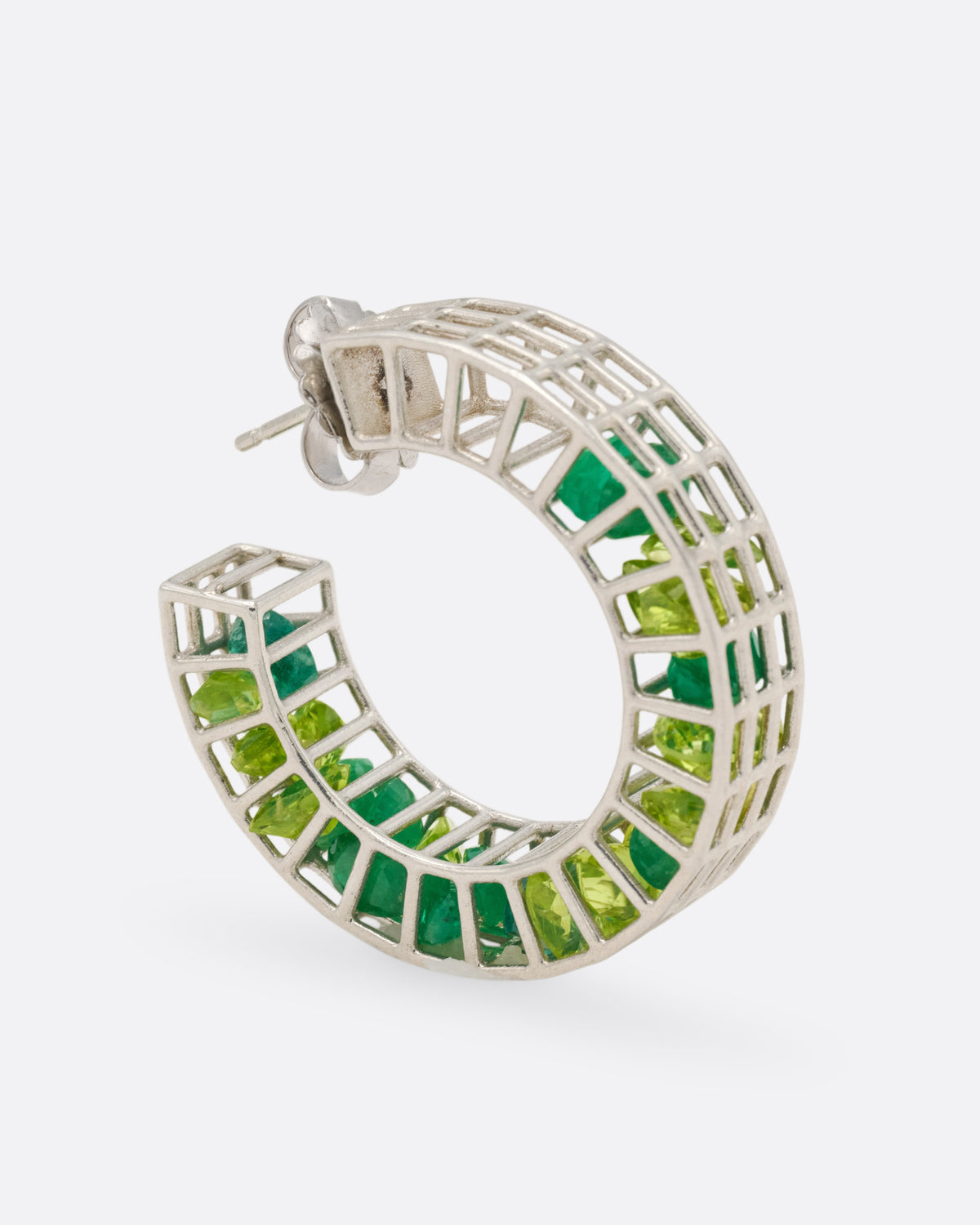 A silver caged hoop earring filled with loose emeralds and peridots, shown from the side standing up.