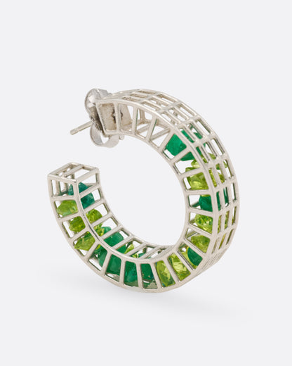 A silver caged hoop earring filled with loose emeralds and peridots, shown from the side standing up.