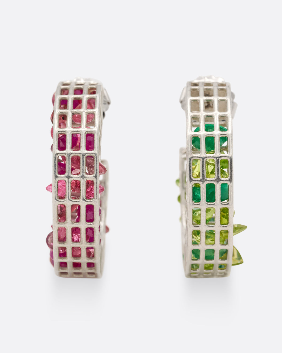 A silver pair of caged hoop earrings filled with loose emeralds, peridots, rubies, and topaz, shown from the front standing up.