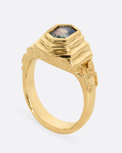 A yellow gold with a stepped center and a portrait cut bicolor tourmaline with a gold tendril that reveals itself through the stone. Shown standing up from the side.