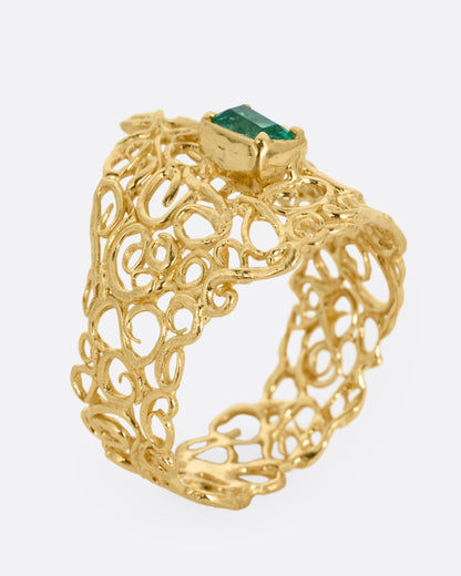 A wide yellow gold curling vine ring with  a central emerald. Shown standing up from the side.