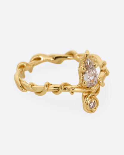 A yellow gold ring with a vine wrapped band and two stacked diamonds, one pear one round. Shown from the alternate side.