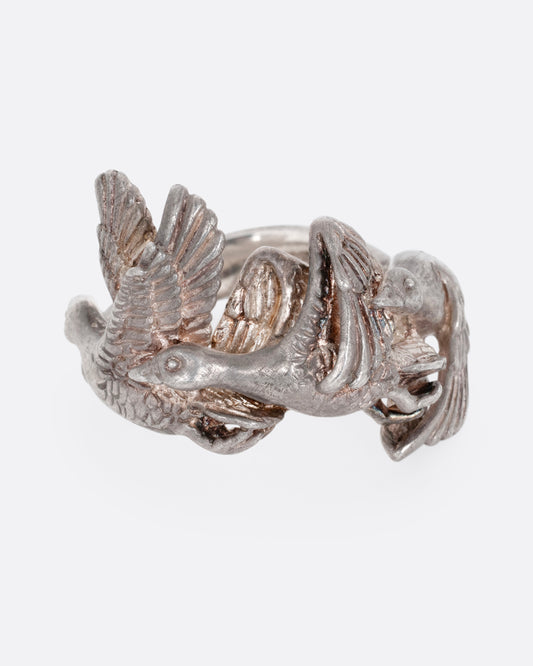 A silver ring with a flock of geese flying along the face. Shown from the front.