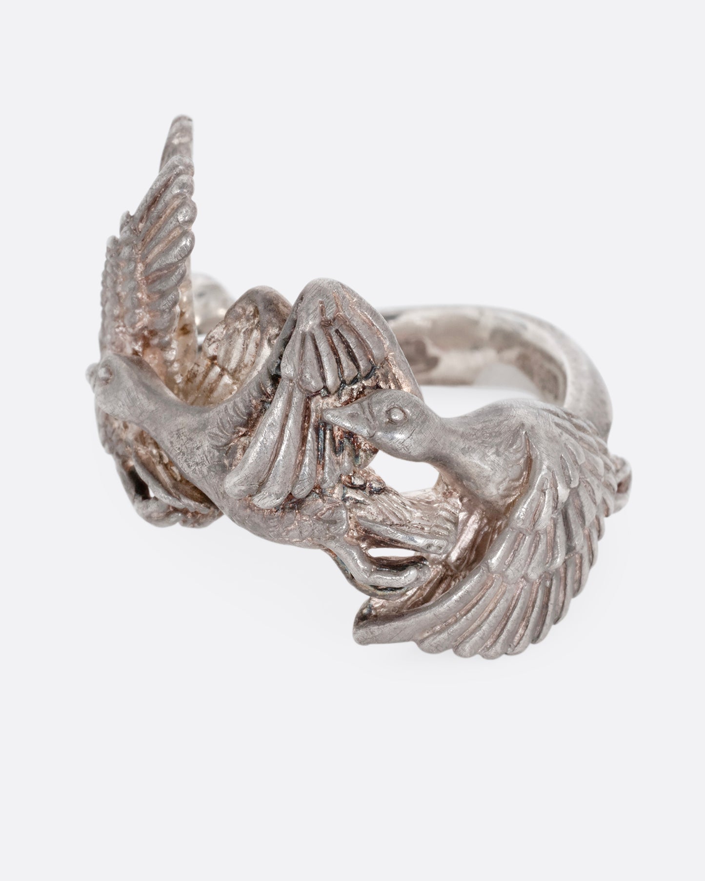 A silver ring with a flock of geese flying along the face. Shown from the side.