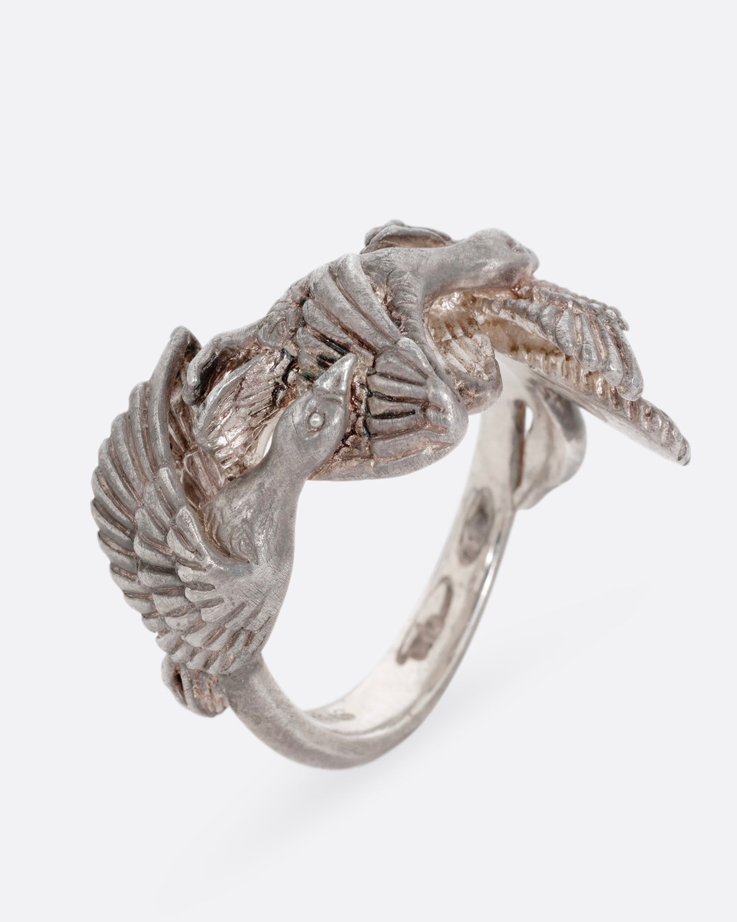 A silver ring with a flock of geese flying along the face. Shown standing up from the side.