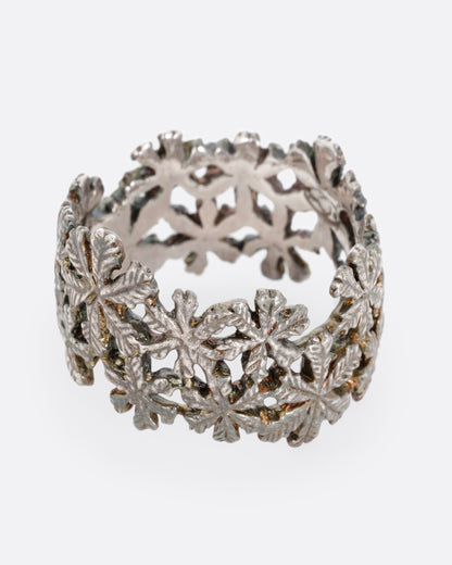 A wide silver ring with a pattern of flowers, shown from the side.
