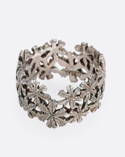 A wide silver ring with a pattern of flowers, shown from the front.