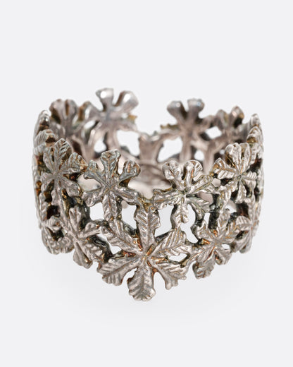 A wide silver ring with a pattern of flowers, shown from the front.