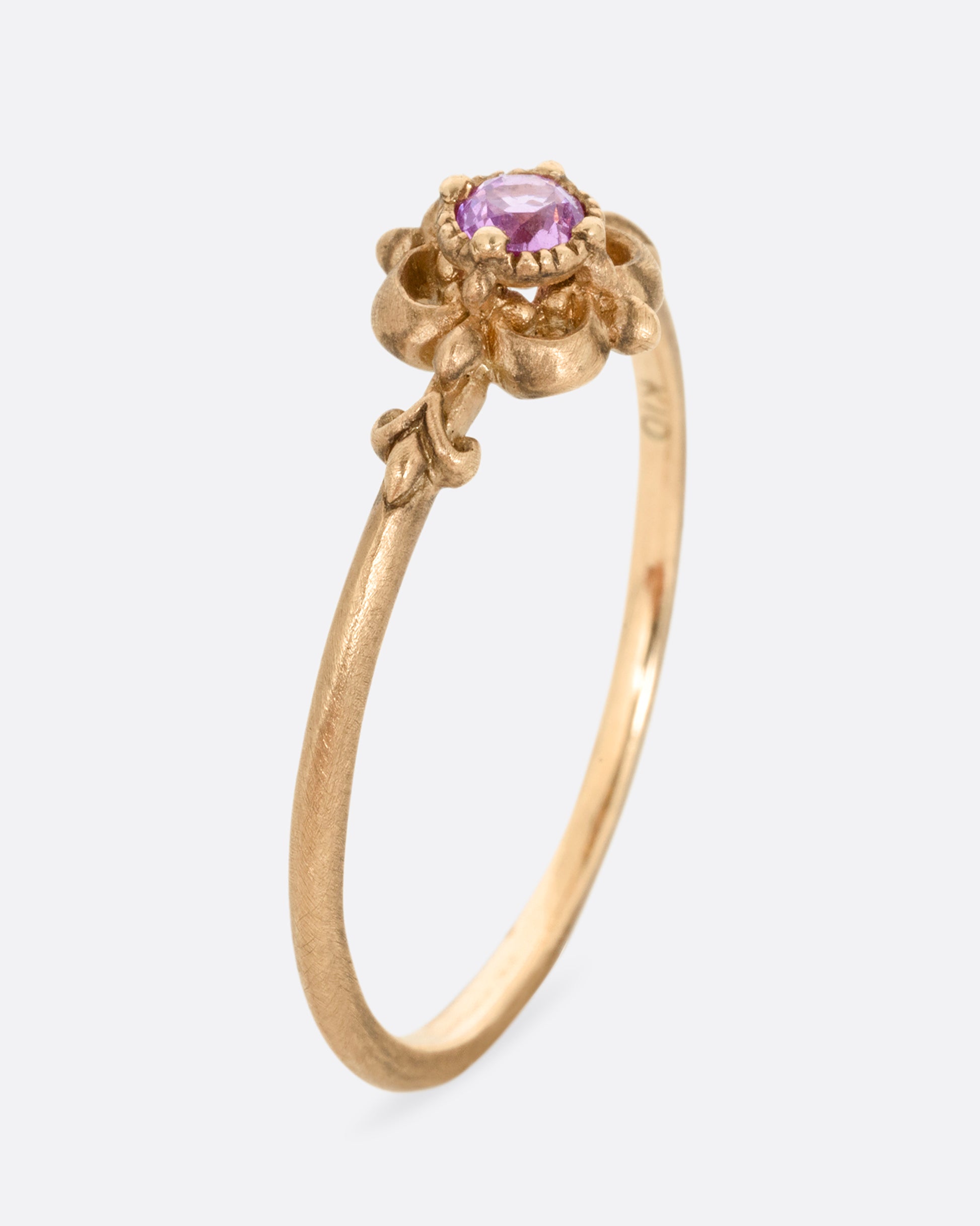 A yellow gold ring with a floral motif and pink tourmaline at the center. Shown from the side standing up.