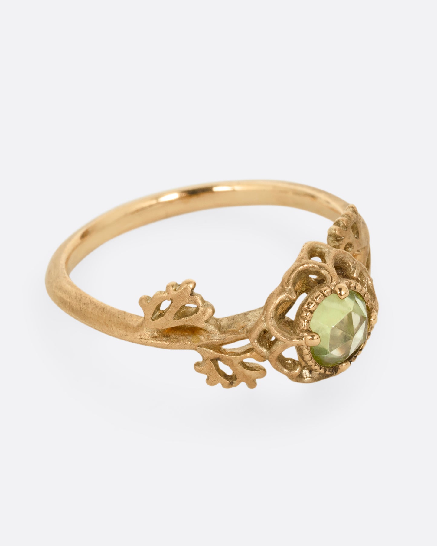 A yellow gold ring with a floral motif and peridot. Shown from the side.
