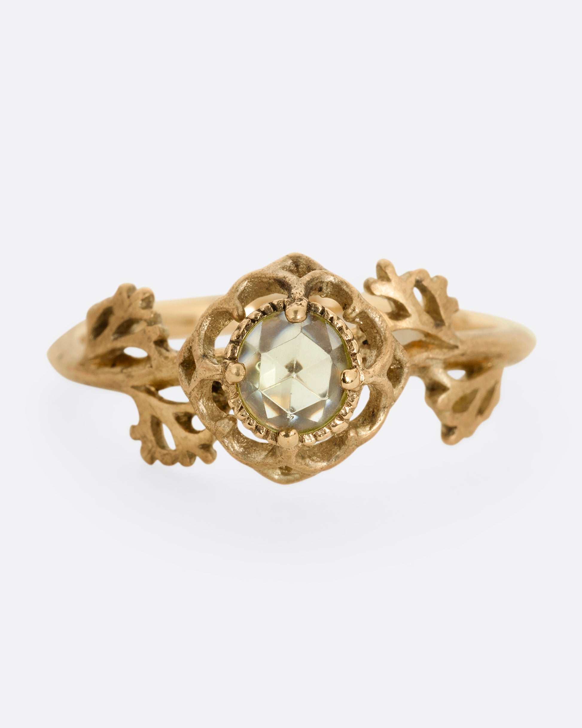 A yellow gold ring with a floral motif and peridot. Shown from the front.