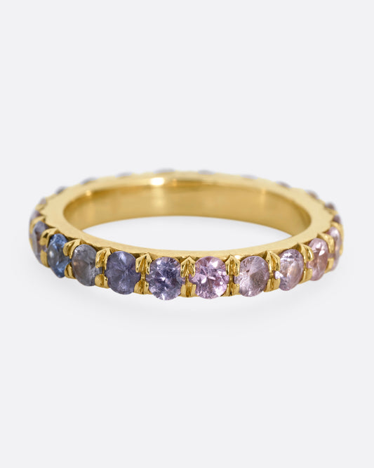 A yellow gold eternity band with multicolored sapphires. Shown from the front.