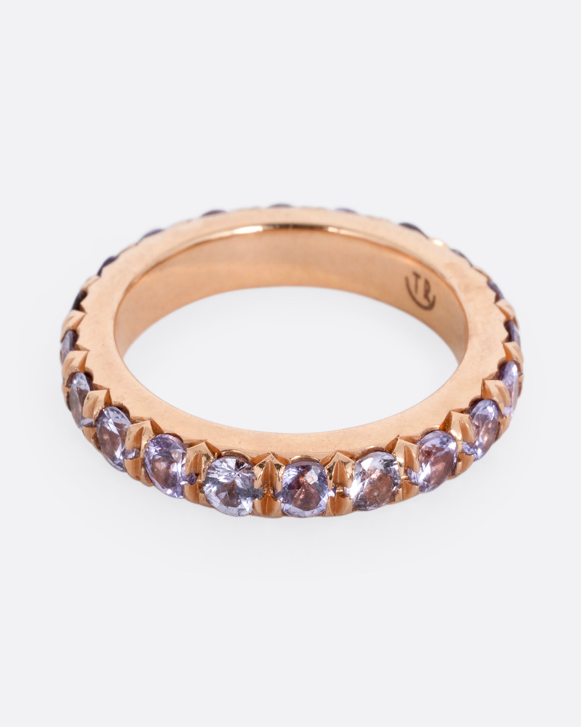 A rose gold eternity ring with lavender sapphires. Shown from the side.