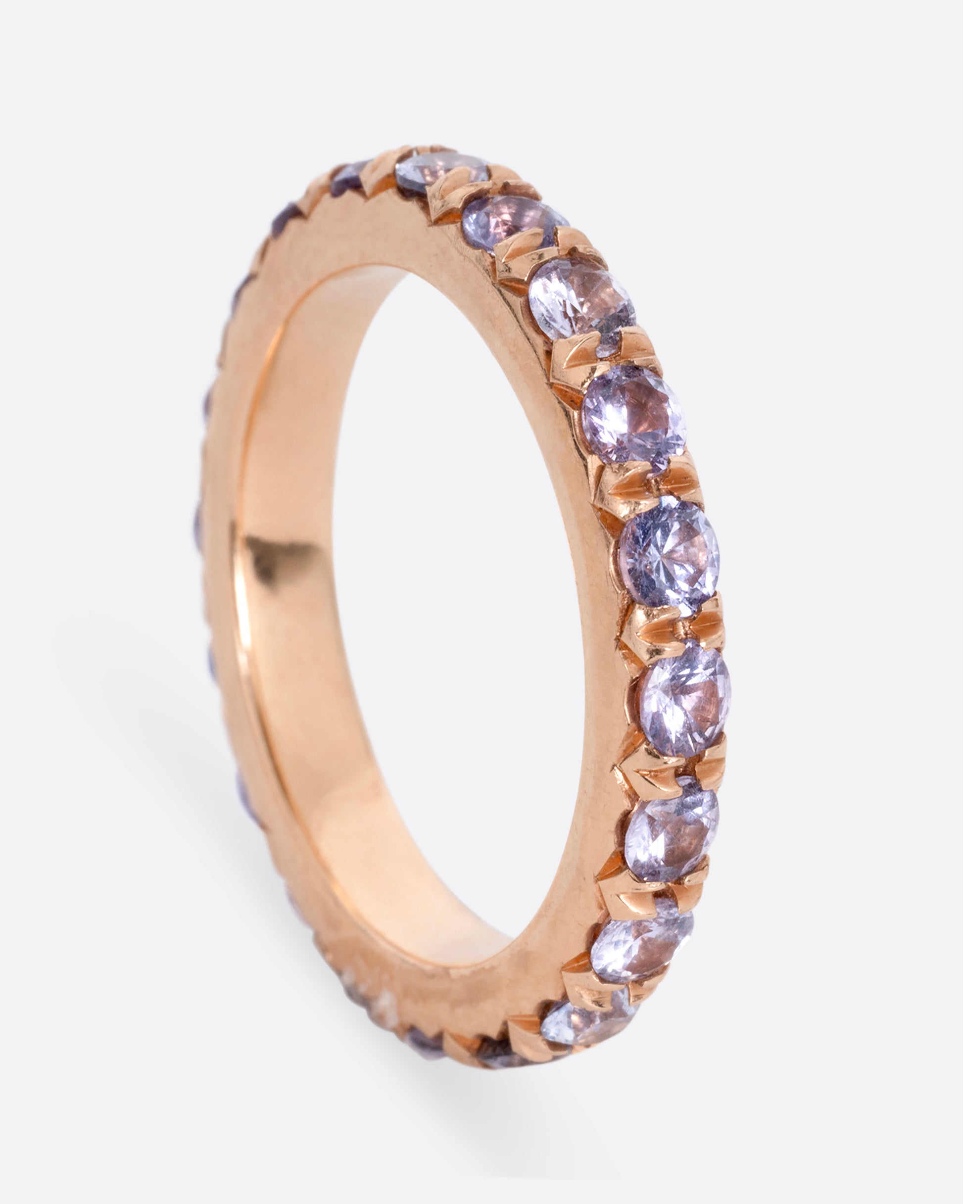 A rose gold eternity ring with lavender sapphires. Shown standing up from the side.