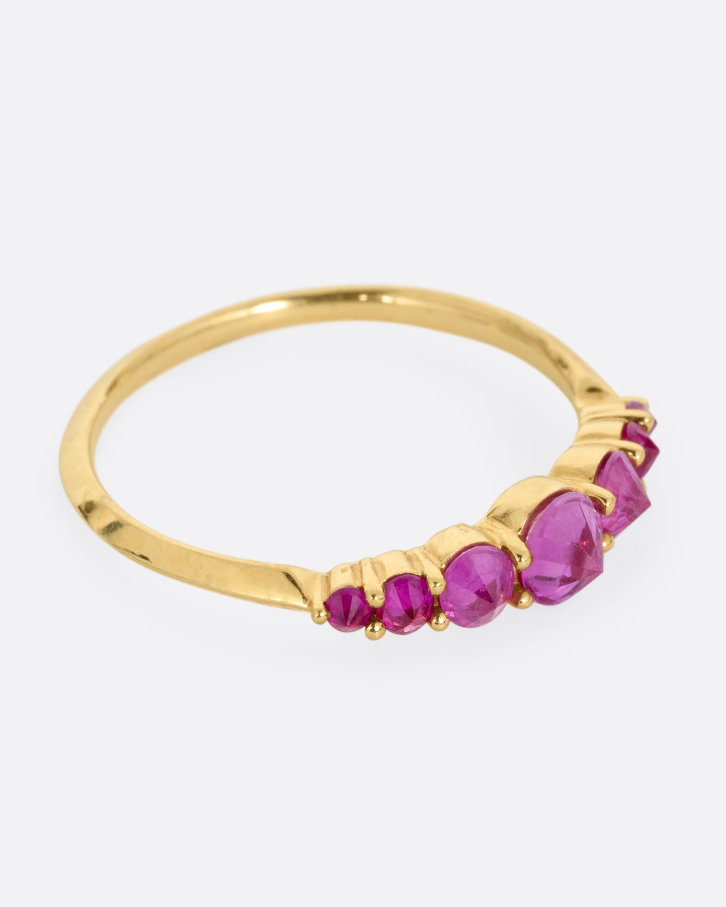 A yellow gold ring with 7 reverse set rubies, shown from the side.